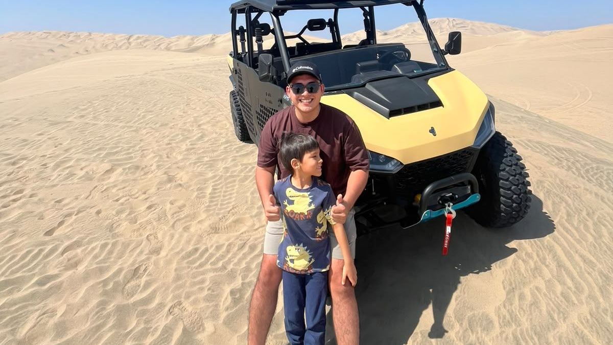 Un padre y su hijo posan delante de un UTV en el desierto de Huacachina